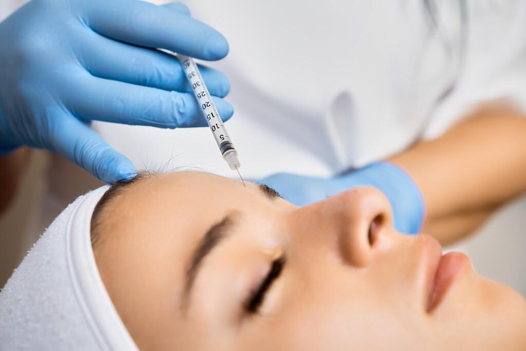 profissional realizando aplicação de harmonização facial na testa de paciente em clínica estética
